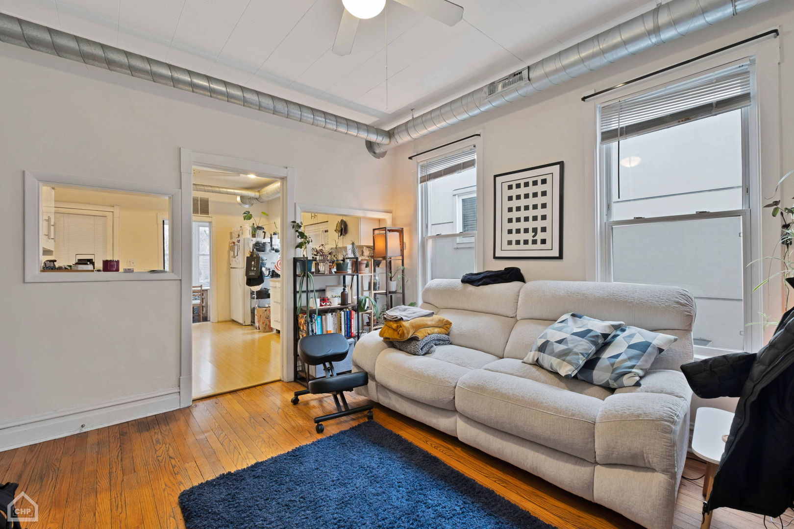 Living room with a cream sectional, hardwood floors, large windows, and exposed ceiling ductwork.