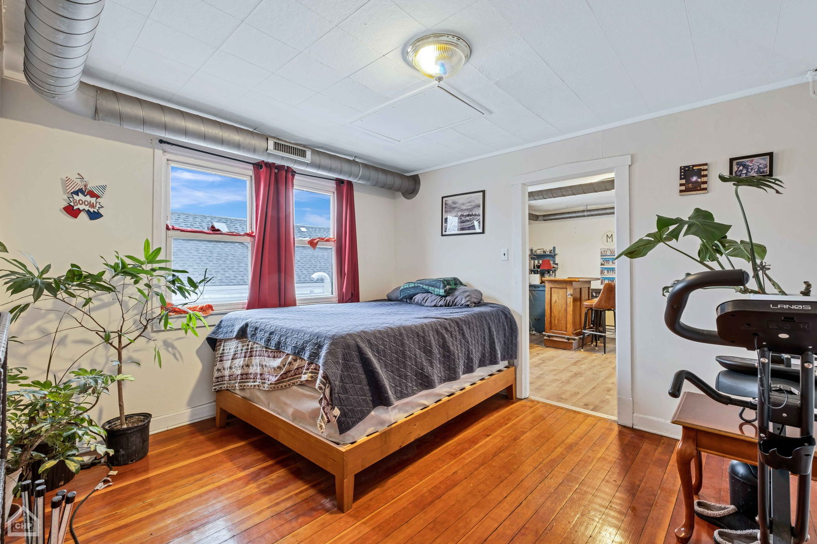 Bedroom with a wooden bed, red curtains, hardwood floors, and exposed ceiling ductwork.
