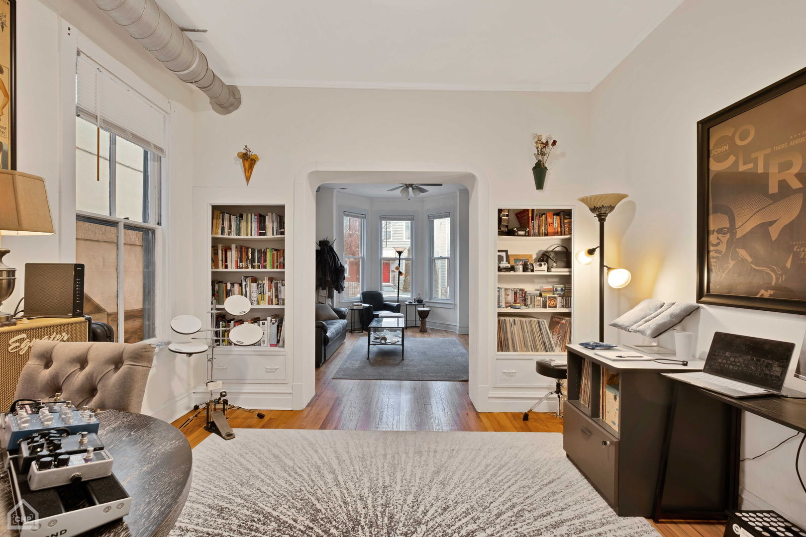 Furnished living room with built-in bookshelves, music equipment, and an arched opening to a bay-window sitting area.