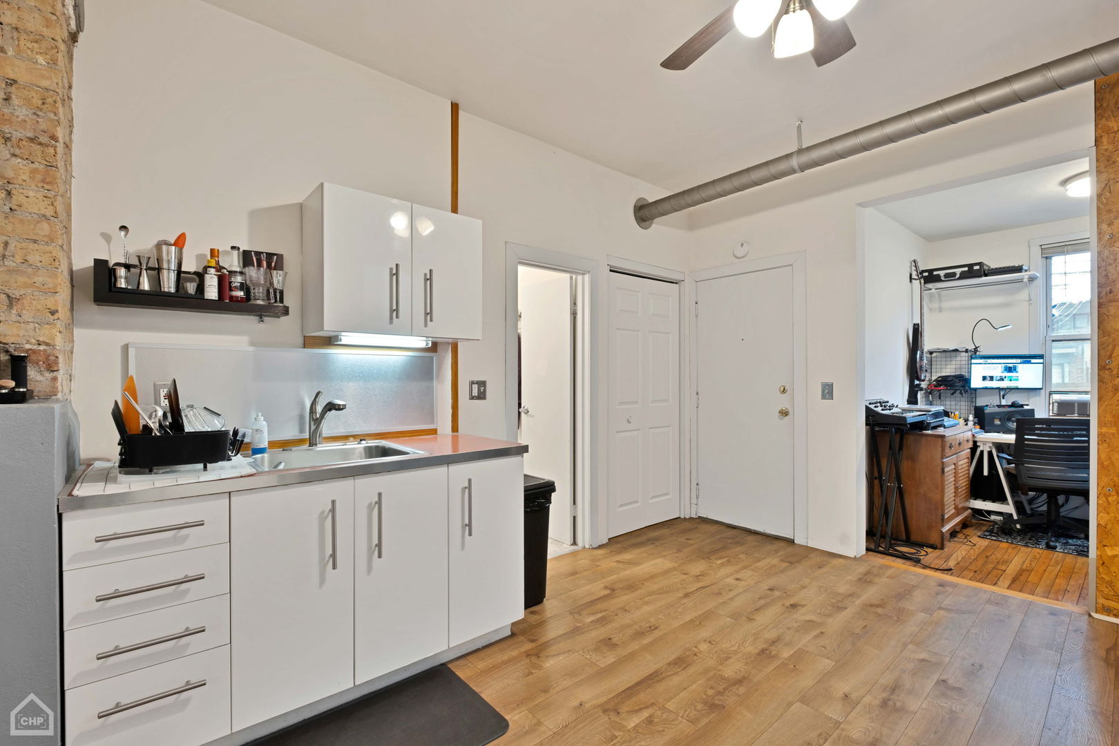 Kitchen with white cabinets, exposed brick, wood floors, and an adjoining office nook.