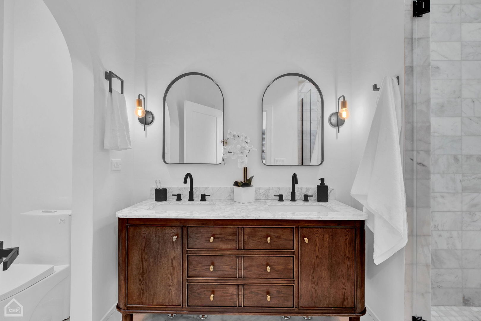 Bathroom with a dark wood double vanity, marble surfaces, and two arched mirrors.
