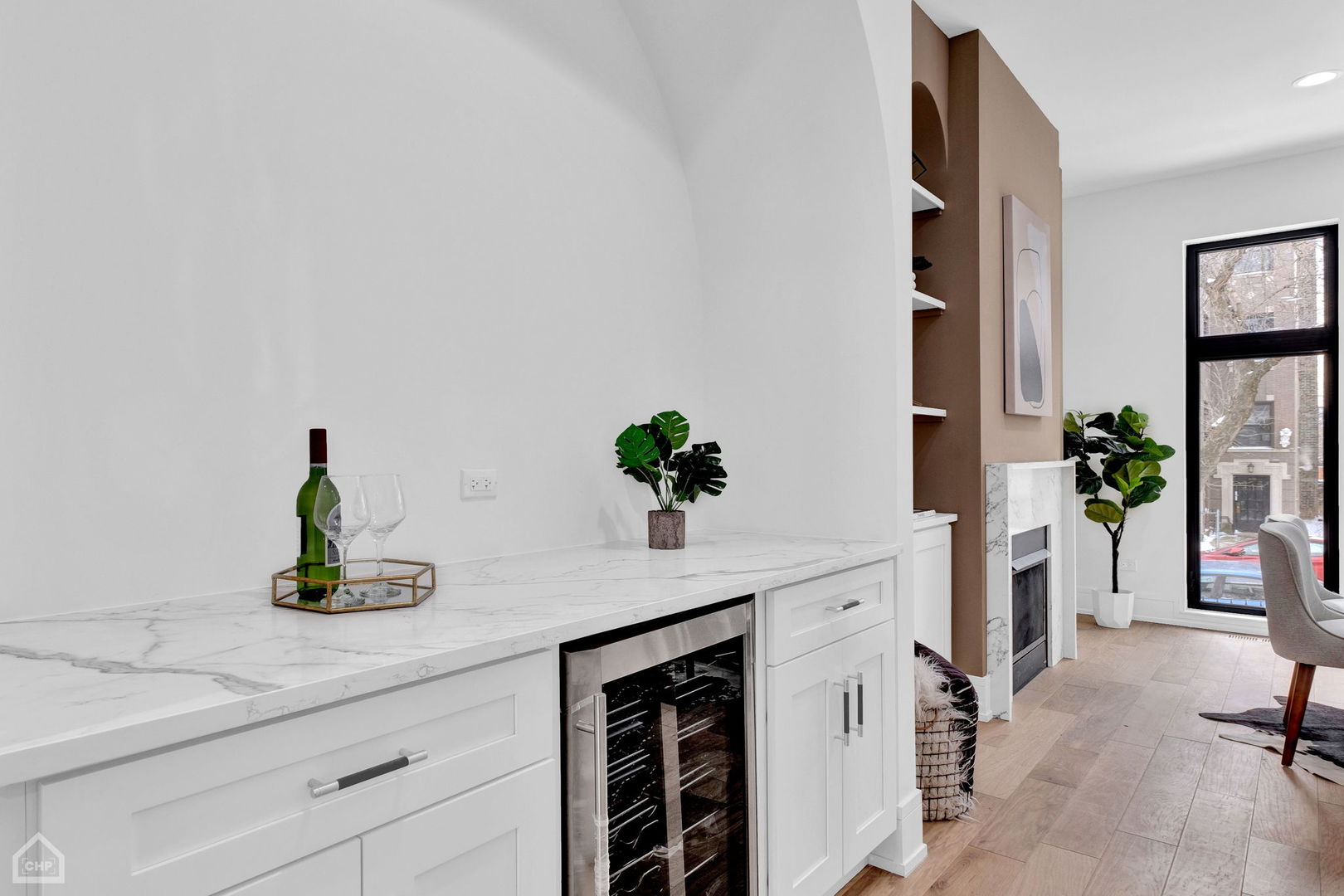 Marble-topped bar with a built-in wine refrigerator beside a fireplace and tall window.
