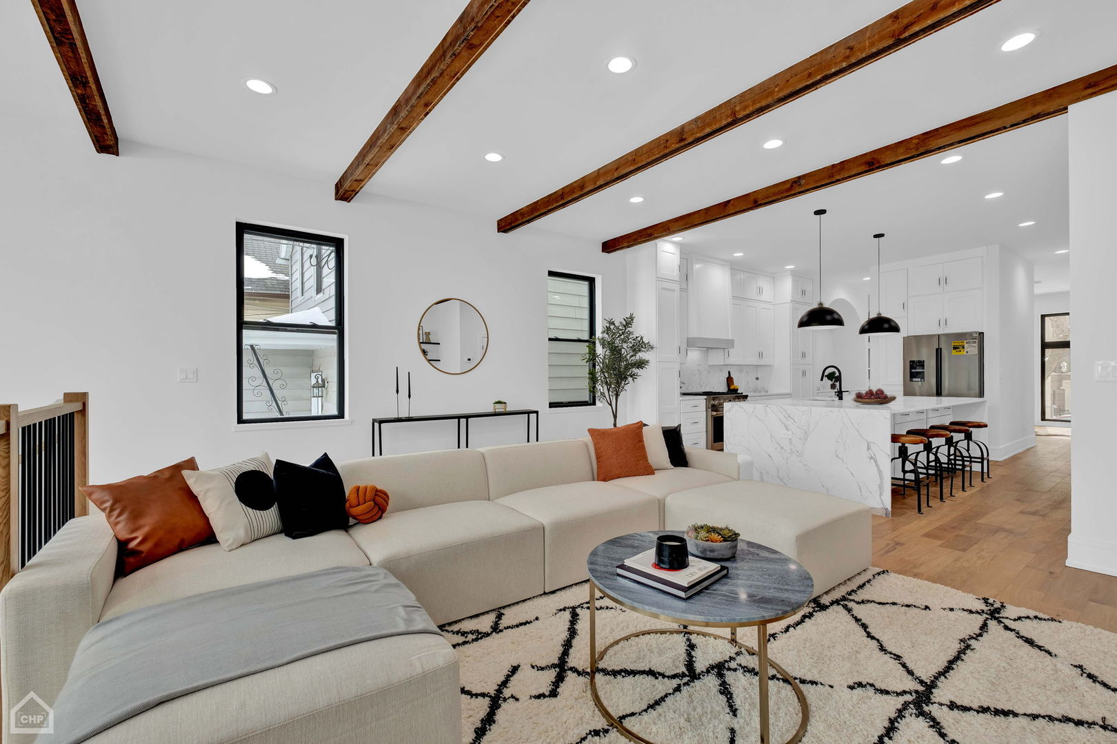 Open-plan living room and kitchen with exposed wood beams and a marble-veined island.