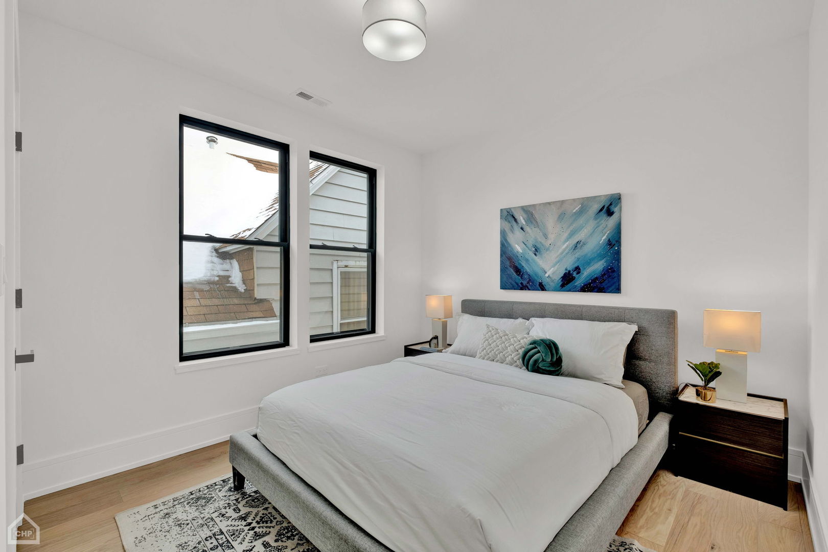 Staged bedroom with a gray upholstered bed, black-framed windows, and blue abstract artwork.