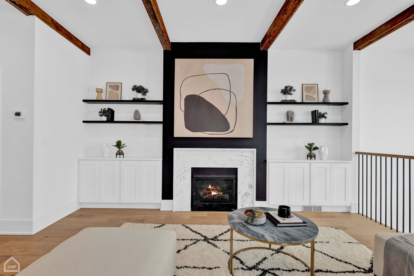 Staged living room with a marble fireplace, built-in shelves, and exposed wood ceiling beams.