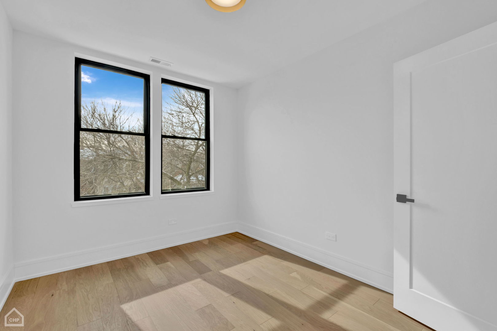 Empty room with light wood floors and two tall black-framed windows.