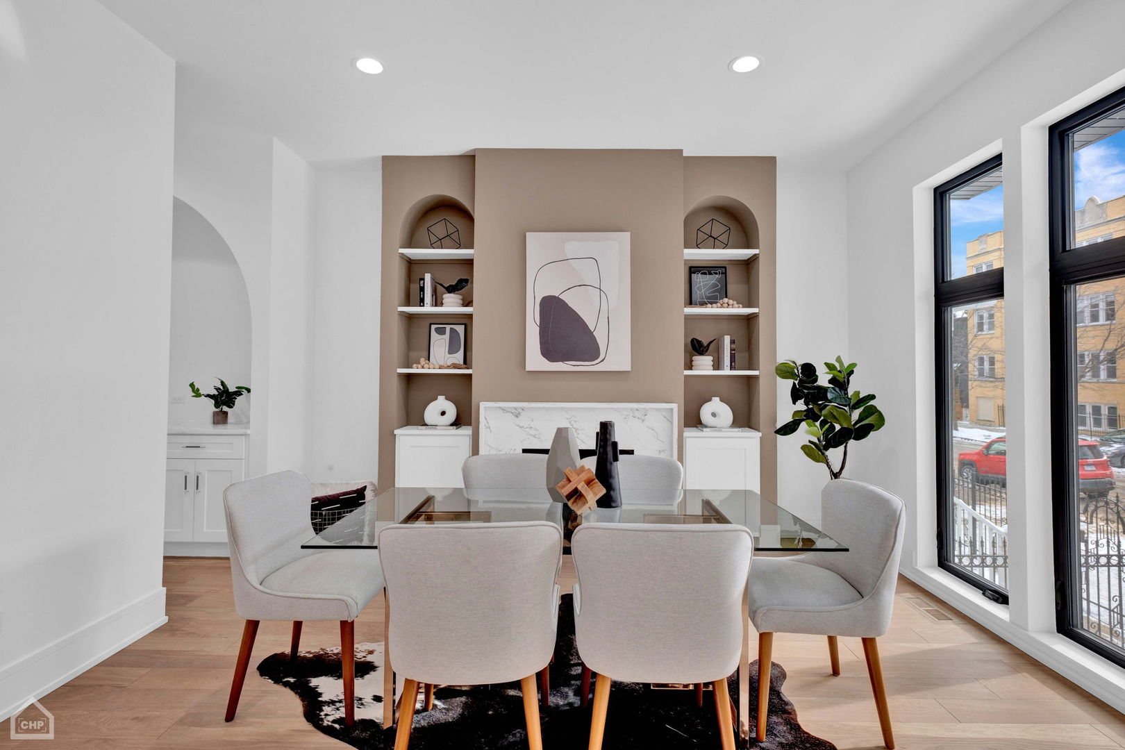 Dining room with a glass-top table, fireplace, built-in shelves, and large street-facing windows.