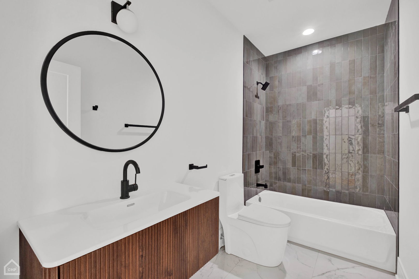 Bathroom with a round black-framed mirror, wood-front vanity, and gray-tiled tub surround.