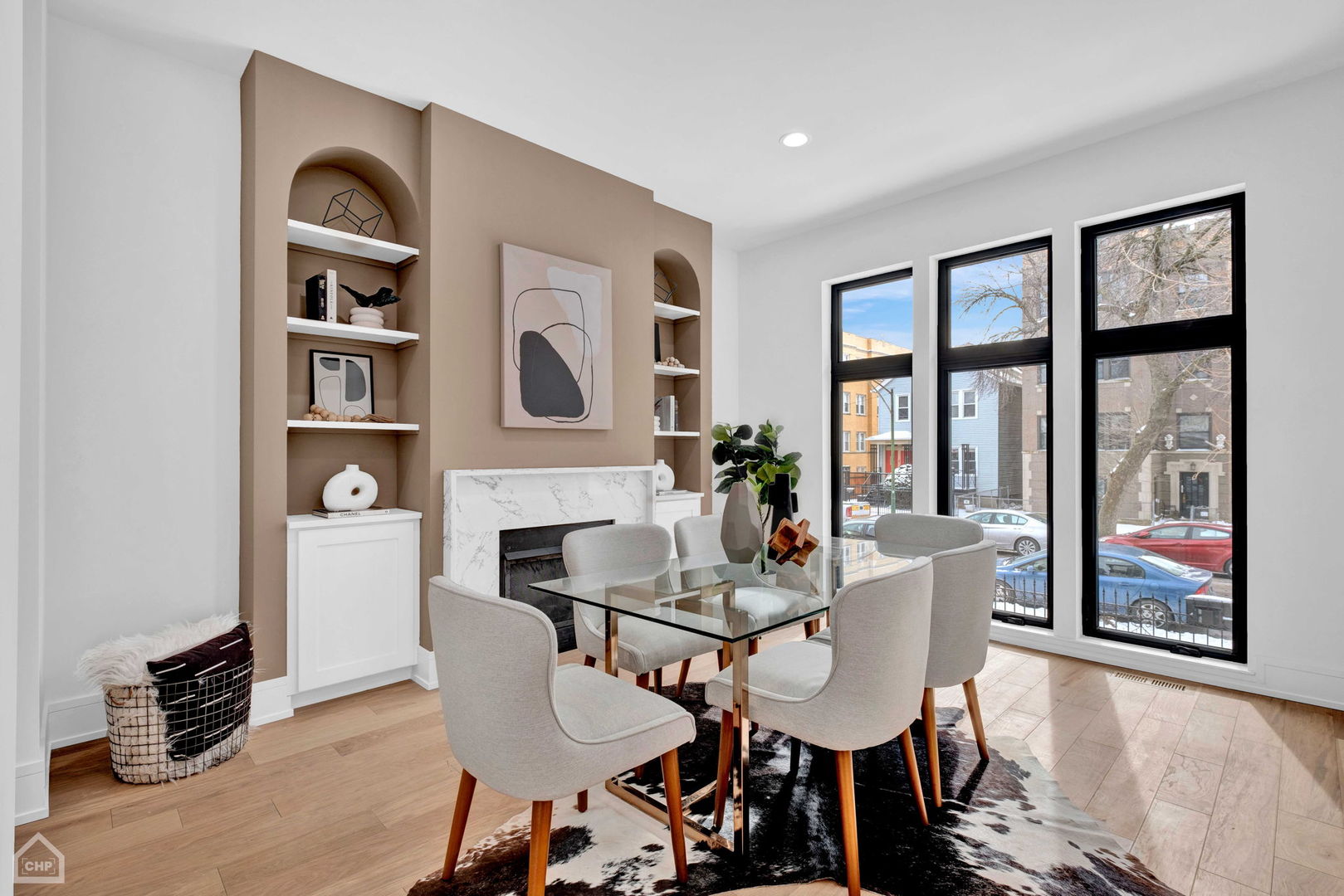 Dining area with a glass-top table, marble fireplace, arched built-ins, and tall street-facing windows.
