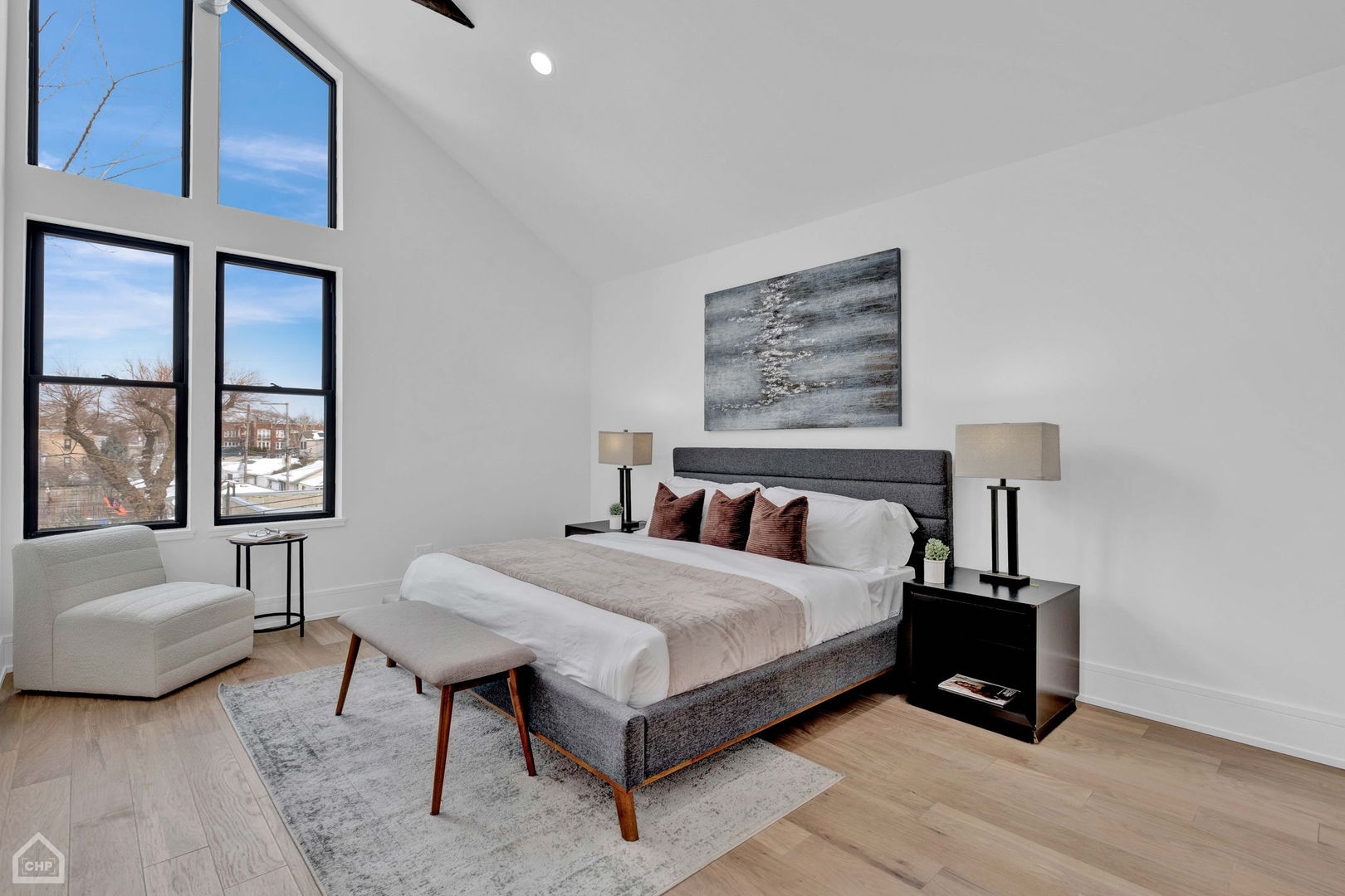 Staged bedroom with a vaulted ceiling, tall windows, and a gray upholstered bed.