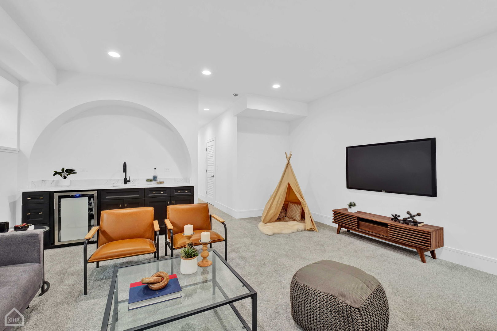 Staged living room with an arched wet bar, leather chairs, and a wall-mounted television.