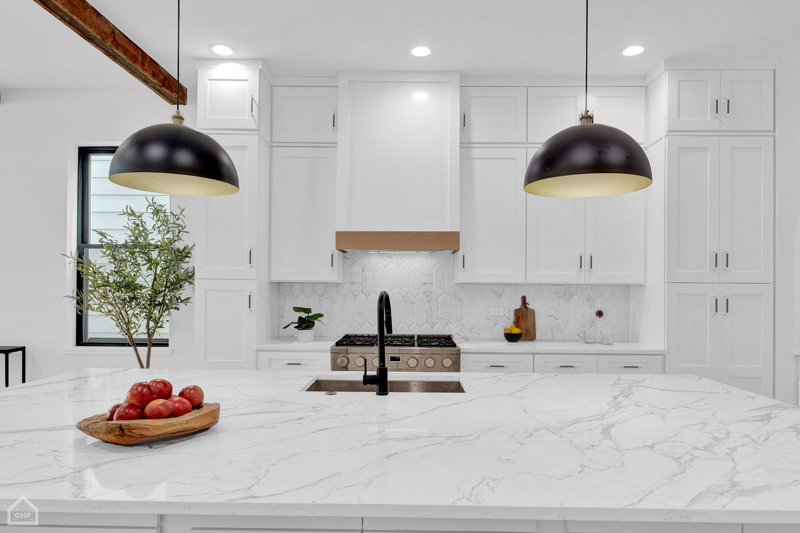 Kitchen with white cabinetry, a veined marble island, black pendant lights, and an exposed wood beam.