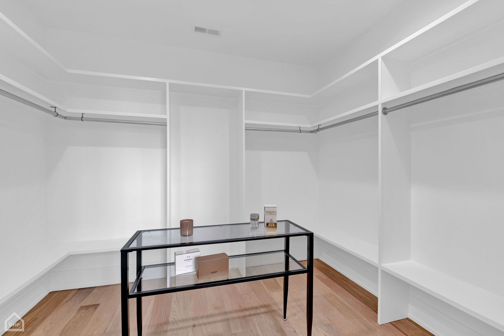 Walk-in closet with white built-in shelving, hanging rods, hardwood floors, and a glass display table.