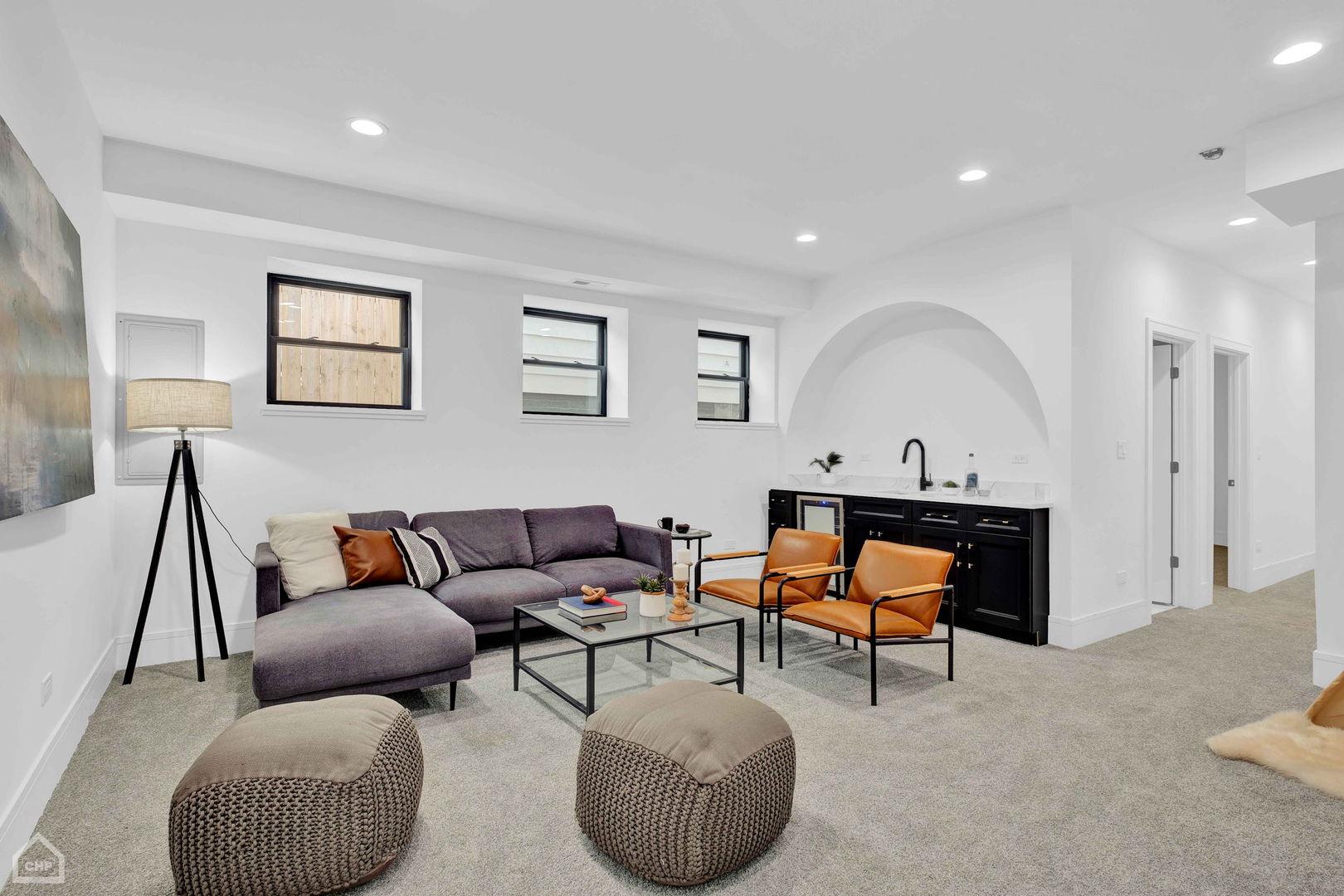 Staged basement living room with a gray sectional, orange chairs, and a black wet bar.