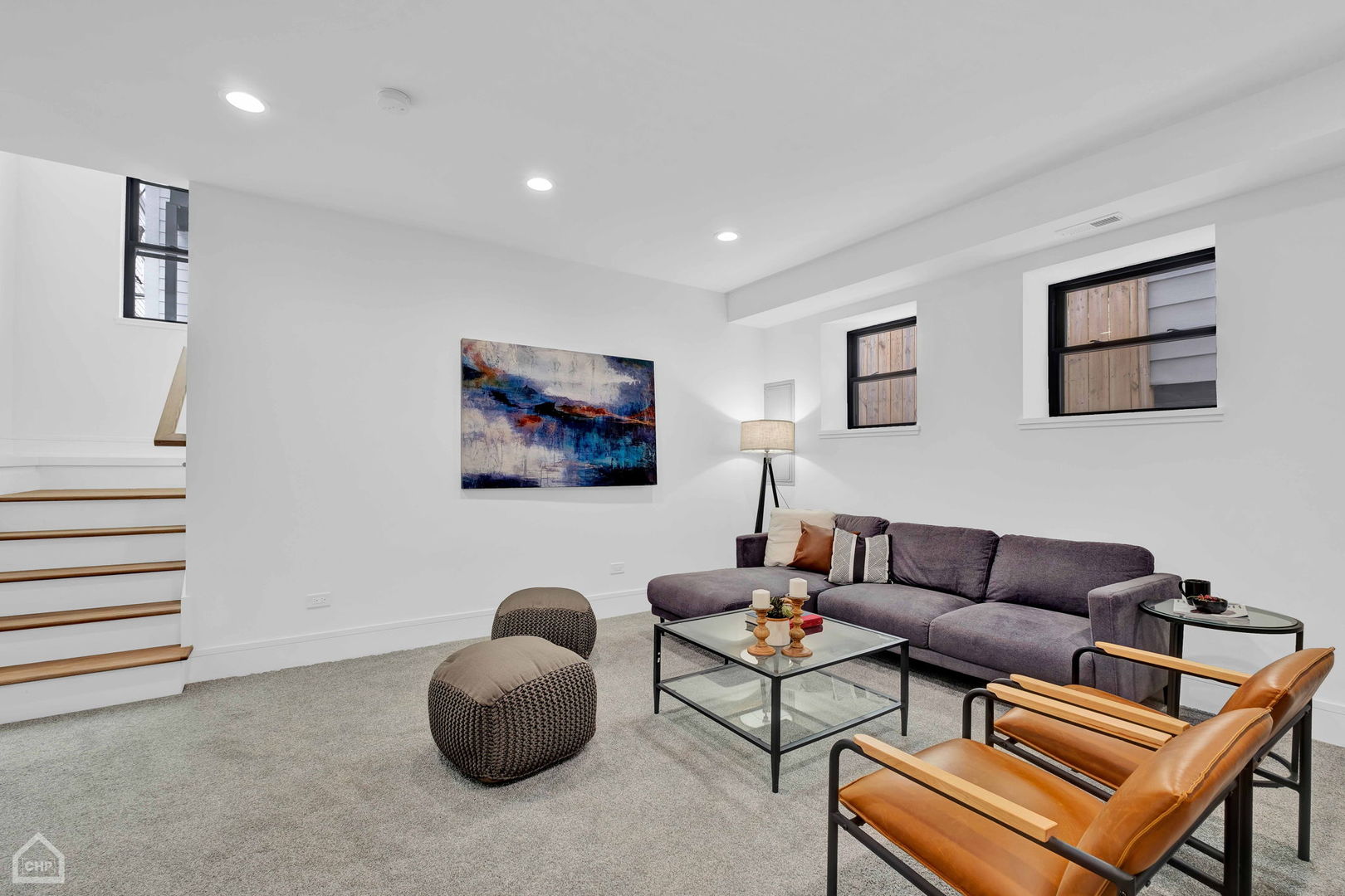 Living room with a gray sectional, leather armchairs, and staircase.
