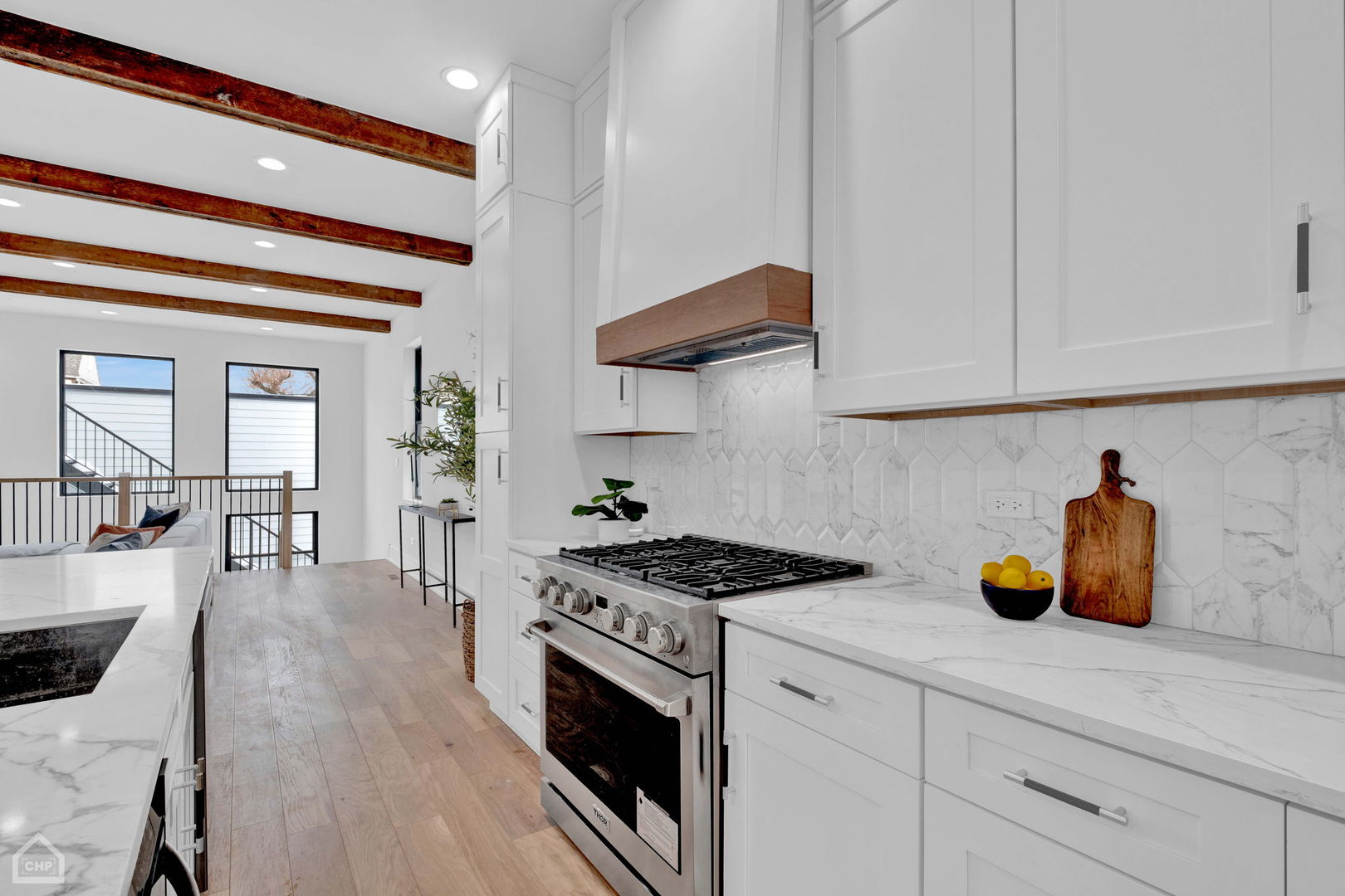 Bright white kitchen with marble counters, a stainless steel range, and exposed wood ceiling beams.
