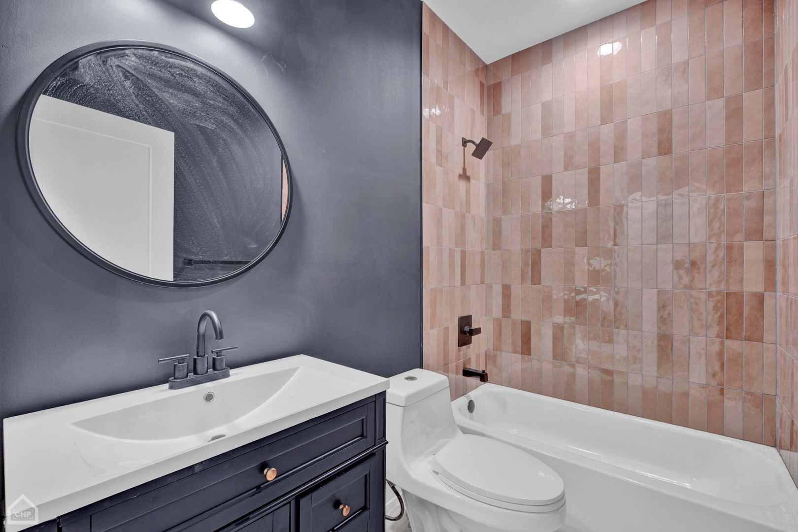 Bathroom with a dark vanity, round mirror, and pink tile surrounding the tub.