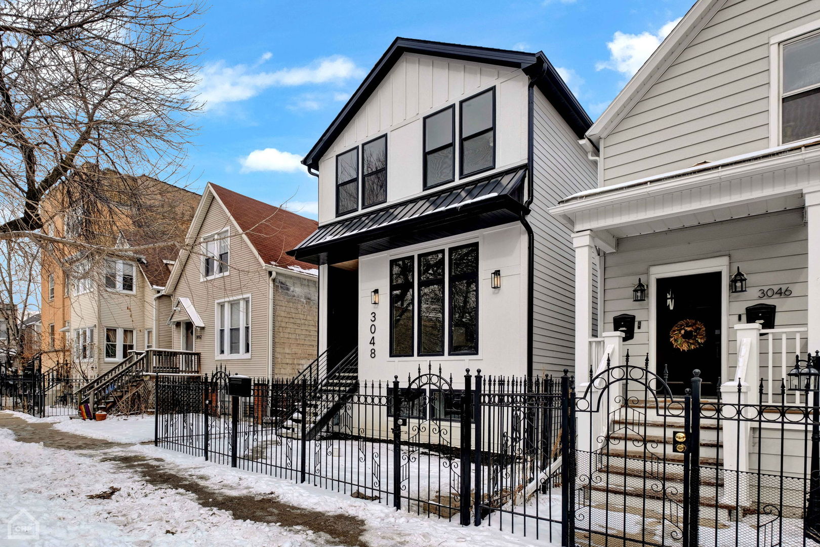 Modern two-story white home with black trim and an iron front fence on a snowy street.