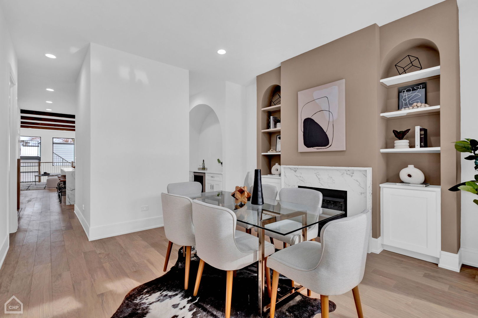 Dining room with a glass table, marble-surround fireplace, and arched built-in shelves.
