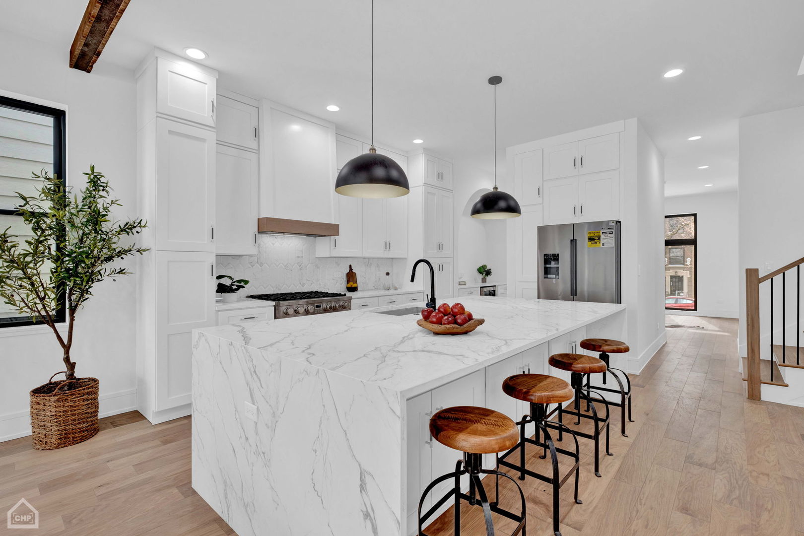 Modern white kitchen with a large veined marble island, wooden bar stools, and black pendant lights.