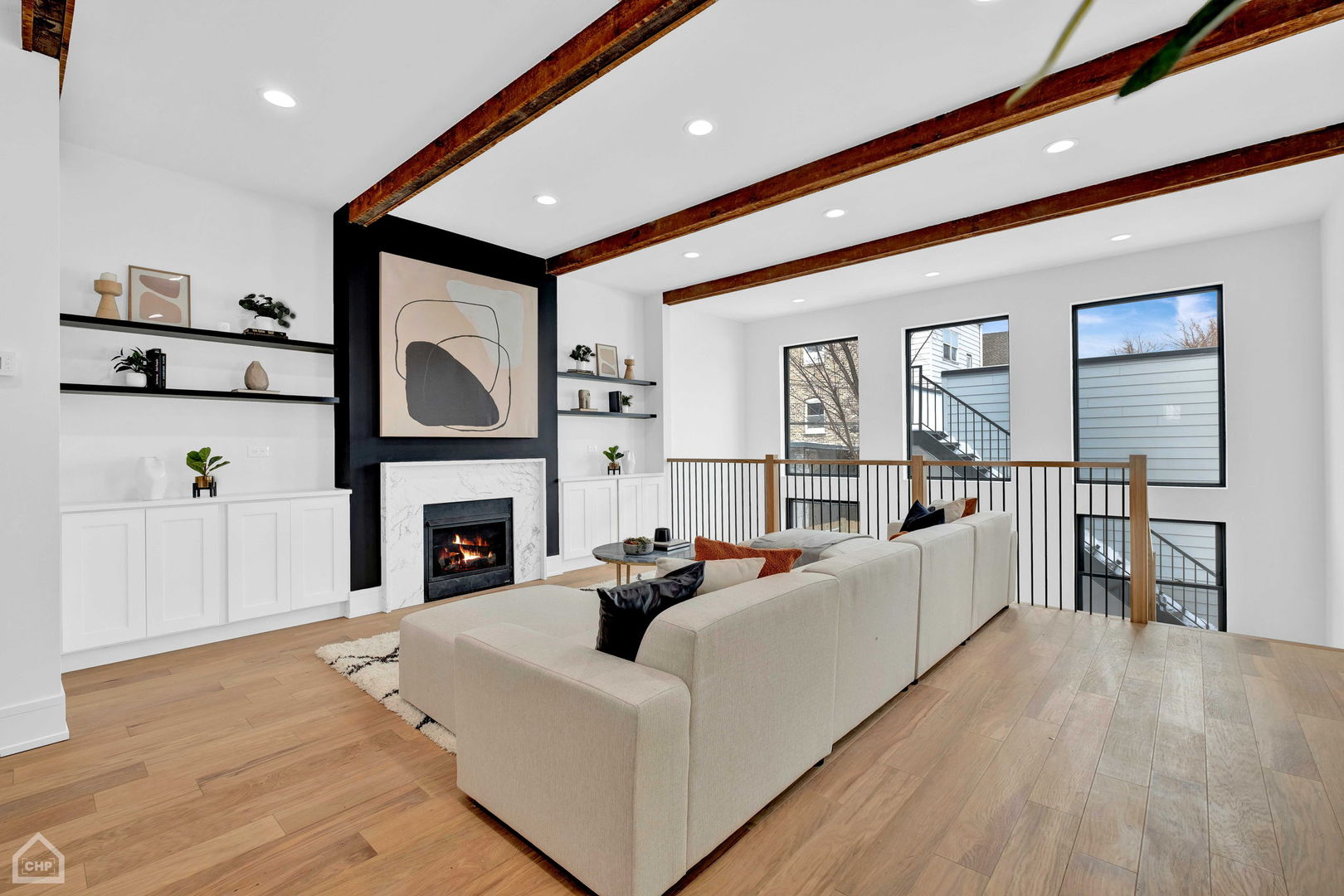 Living room with exposed wood beams, marble fireplace, built-ins, and a sectional beside an open stairwell.