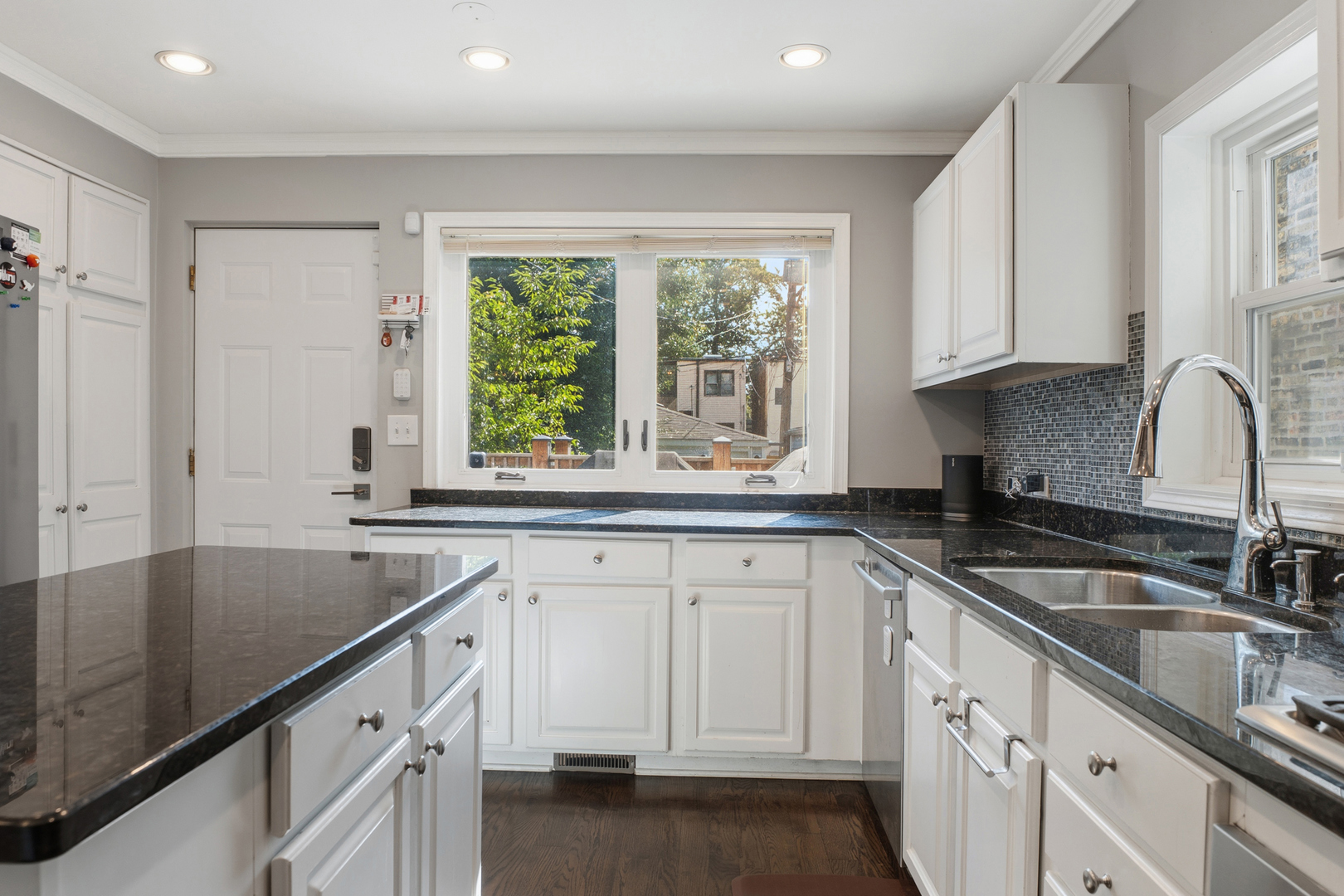 Kitchen with white cabinets, dark stone island and counters, and a wide window overlooking trees.