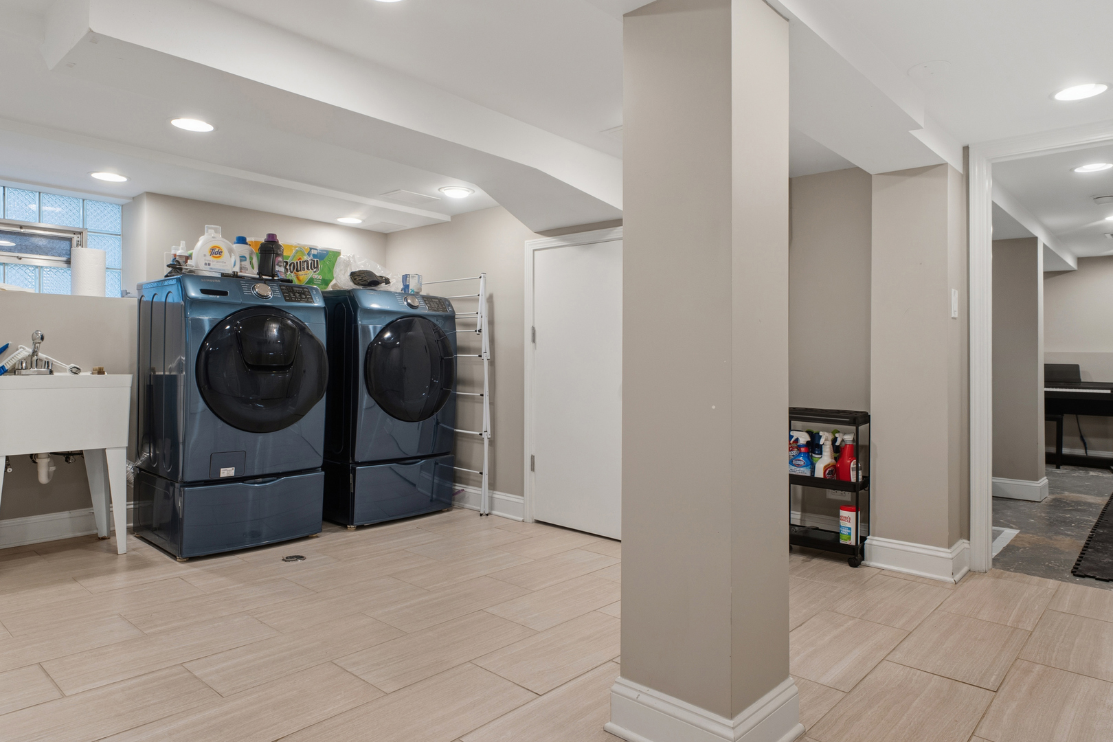 Basement laundry room with dark blue washer and dryer beside a utility sink.