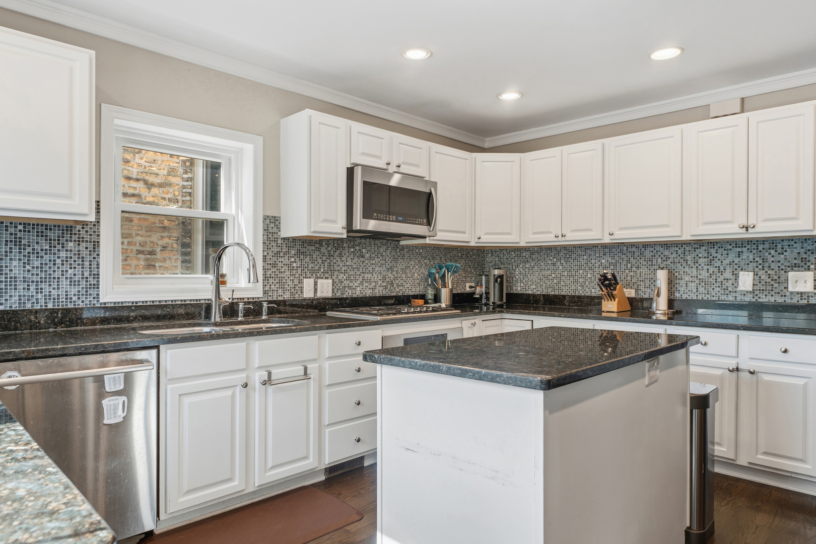 Kitchen with white cabinets, dark stone counters, mosaic tile backsplash, and a central island.