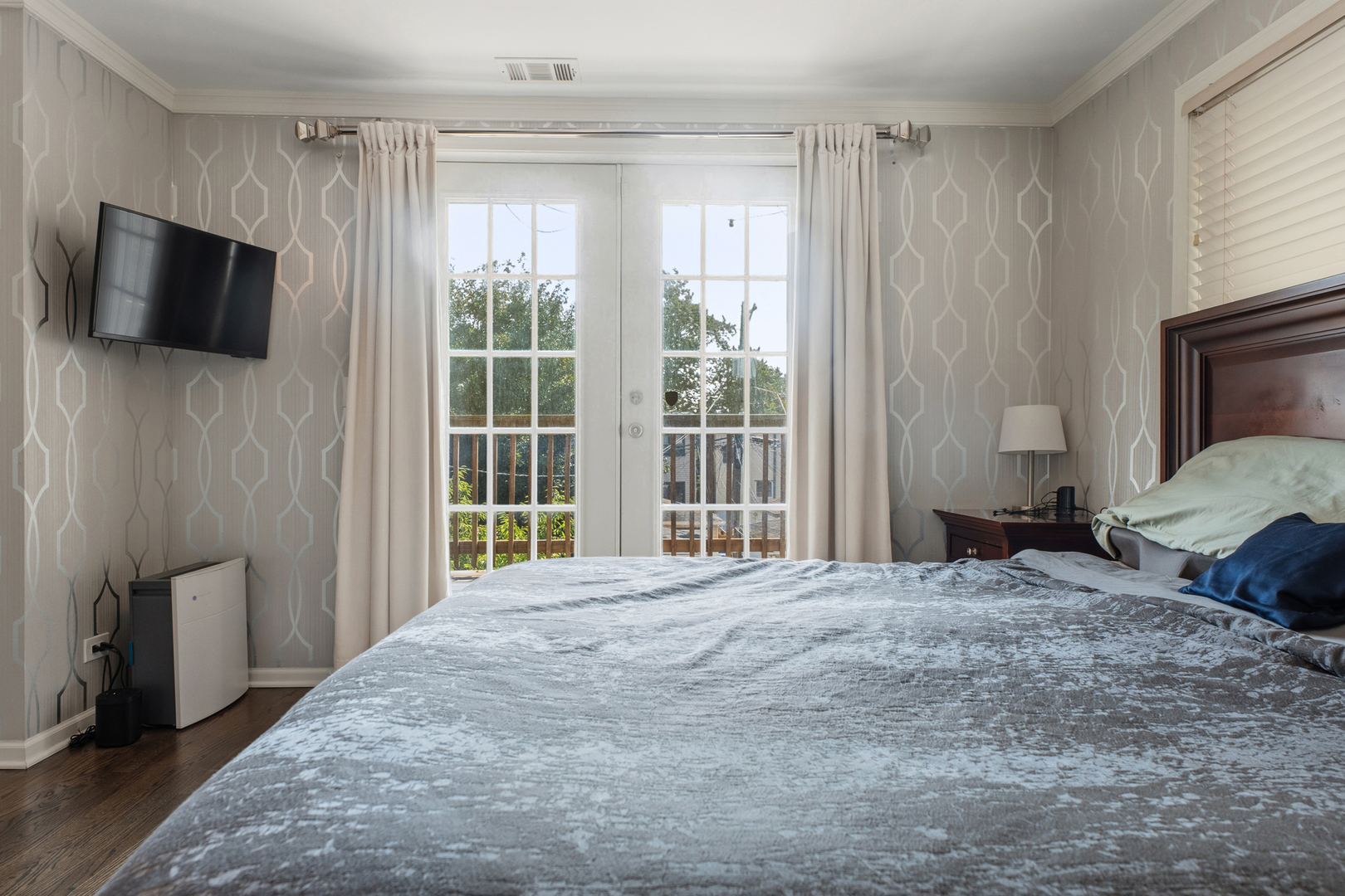 Bedroom with a large bed, patterned wallpaper, and French doors overlooking a deck.