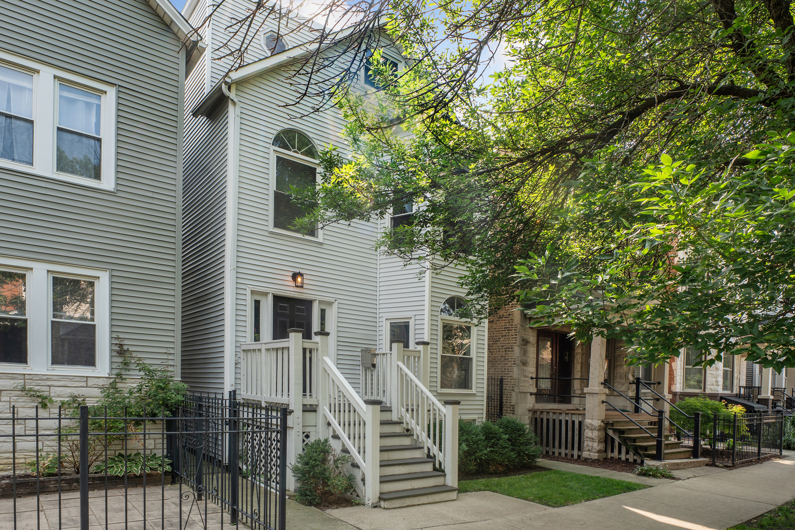 Light-sided two-story home with a raised entry, white stairs, and leafy trees shading the facade.