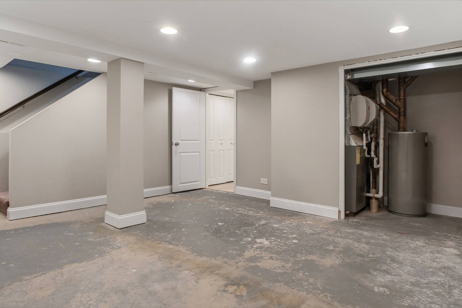 Unfinished basement with concrete floor, staircase, and exposed furnace and water heater.