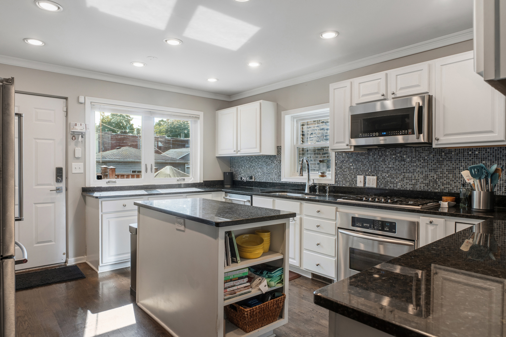 Kitchen with white cabinets, dark granite counters, mosaic backsplash, stainless appliances, and a central island.
