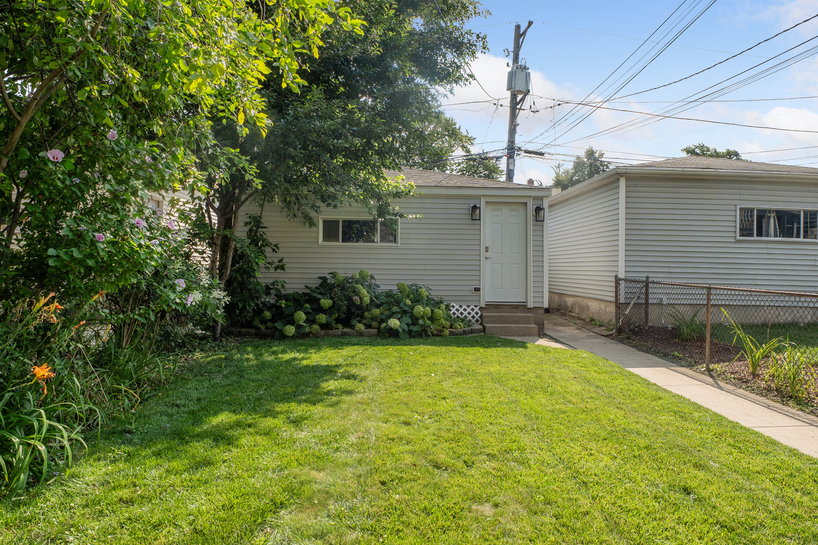 Single-story house with a white entry door, shaded garden, and broad green lawn.
