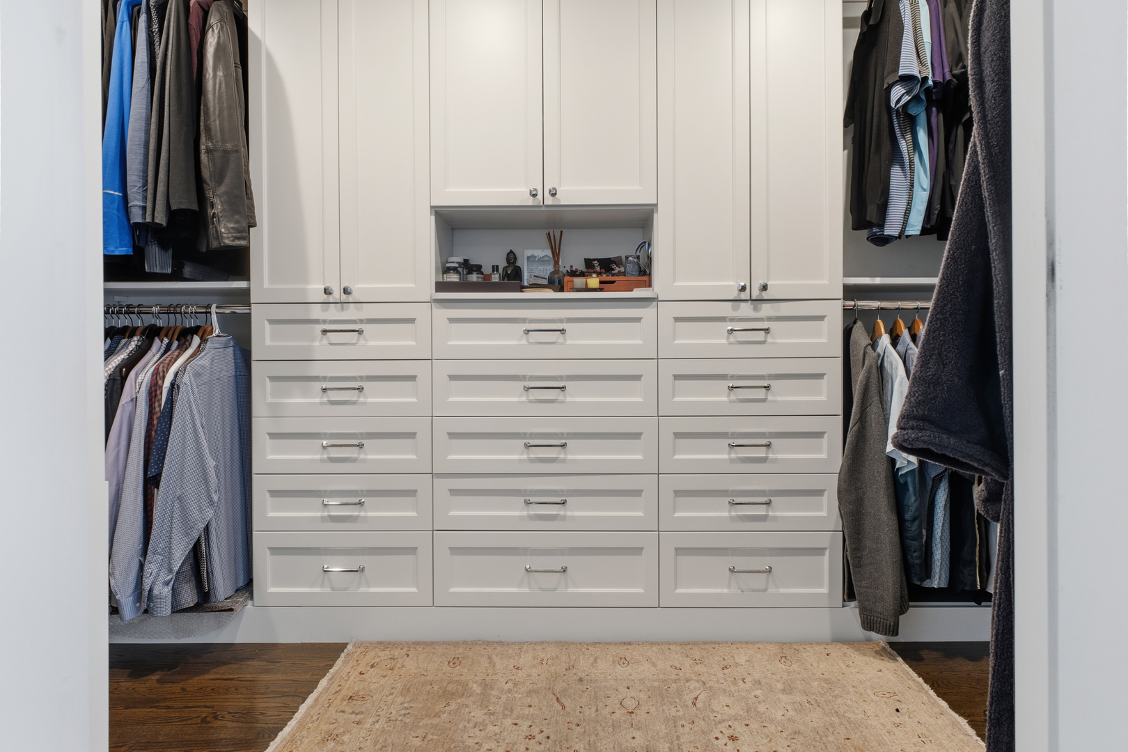 Walk-in closet with white built-in drawers, open clothing racks, and a patterned rug.