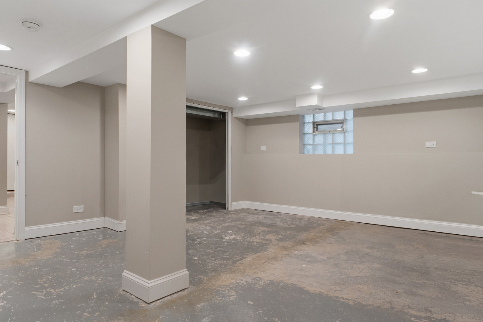 Basement room with a concrete floor, central support column, and glass-block window.