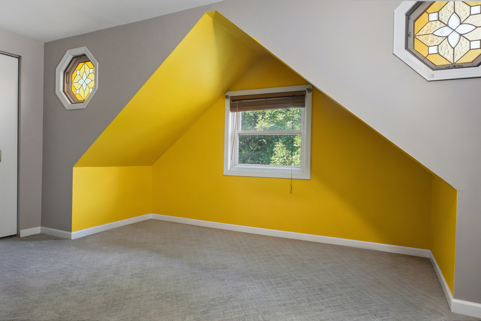 Empty attic room with bright yellow walls, a sloped ceiling, gray carpet, and decorative stained-glass windows.
