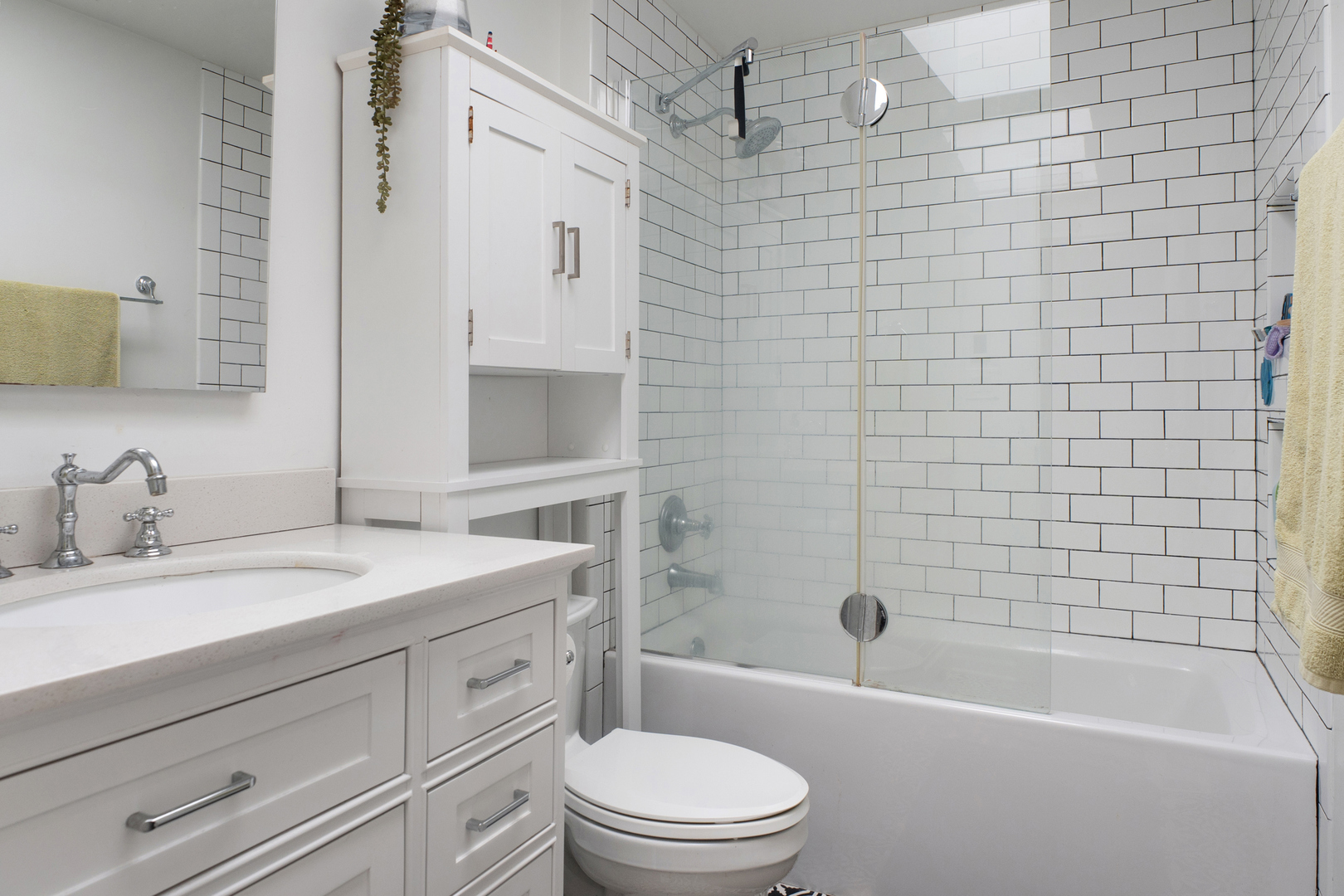 Bathroom with a white vanity and a glass-enclosed bathtub and shower lined with subway tile.