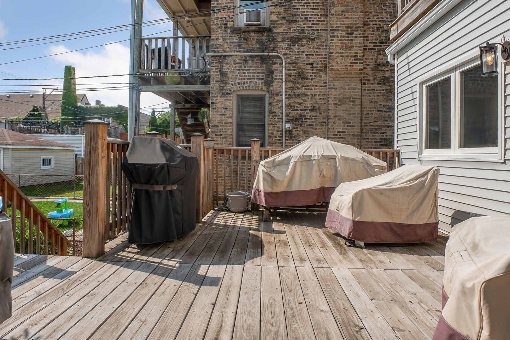 Elevated wooden deck with railings, stairs, a covered grill, and covered outdoor furniture.