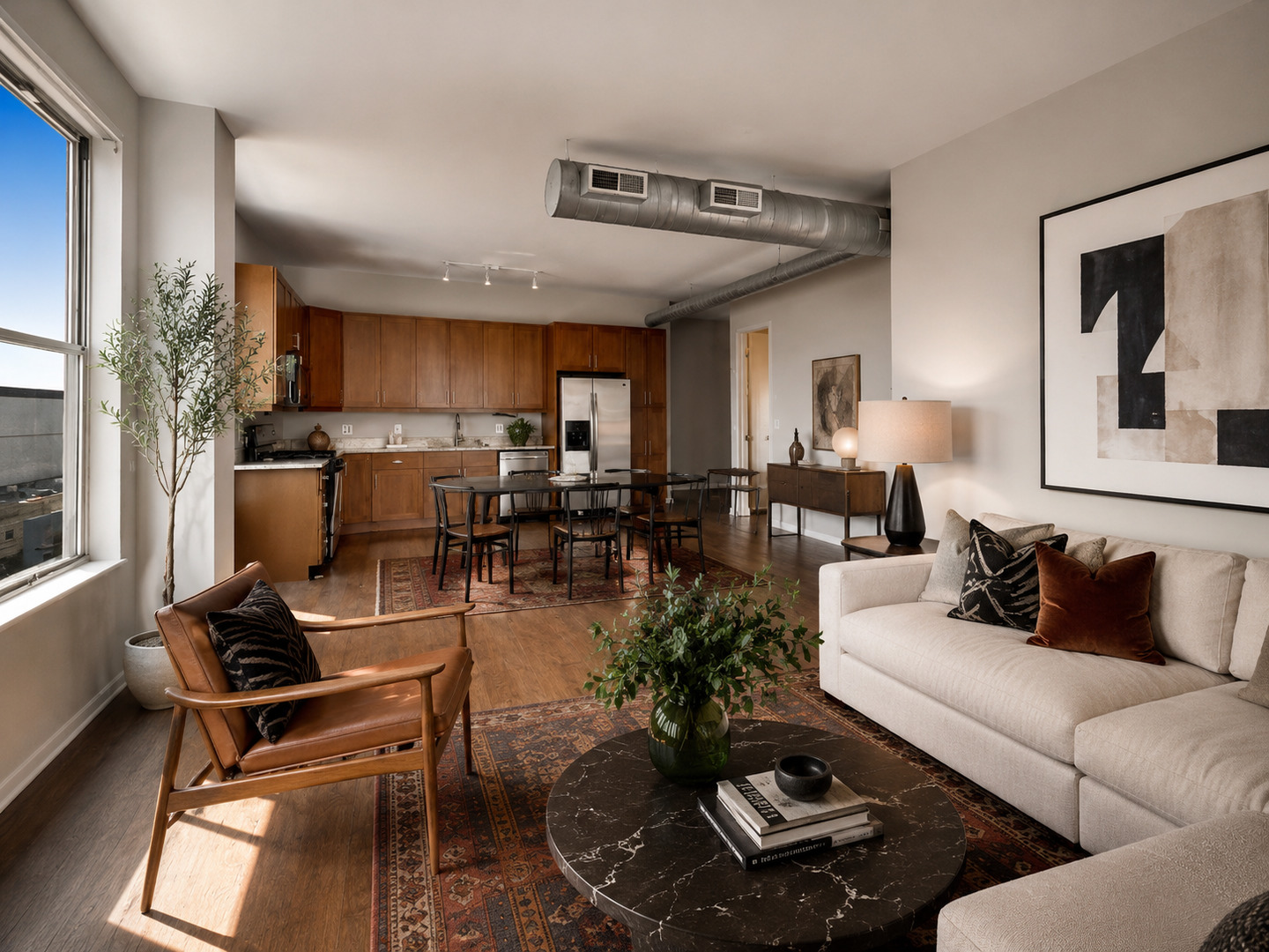 Open-plan condo living room with a cream sofa, leather armchair, and adjoining wood-cabinet kitchen.