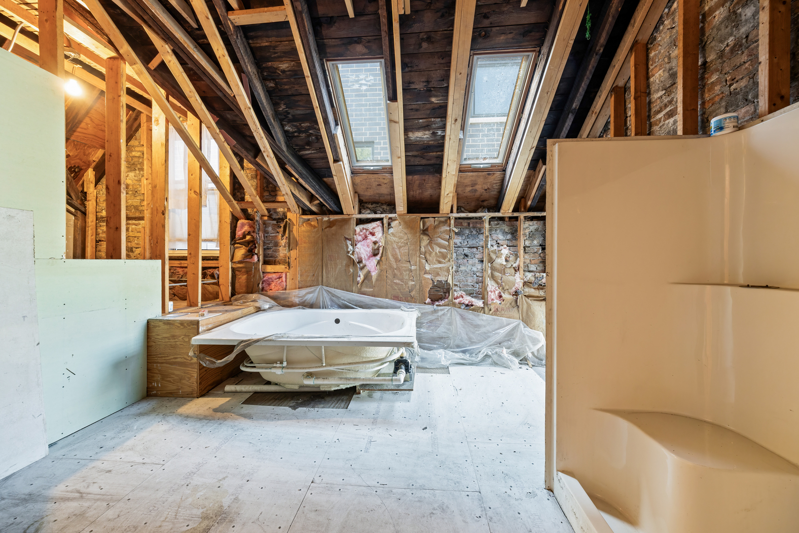 Unfinished attic bathroom with exposed rafters, two skylights, and a jetted tub.
