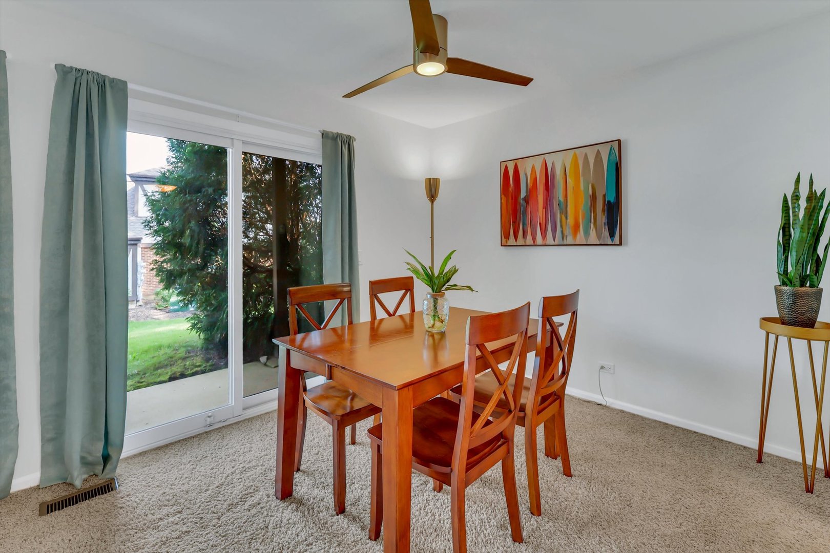 Dining room with a wooden table, teal curtains, and sliding glass doors overlooking a lawn.