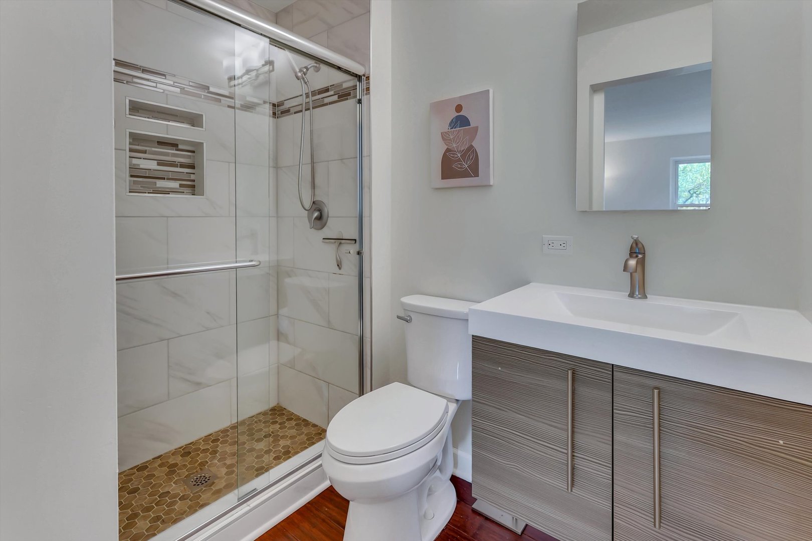 Bathroom with a glass walk-in shower, hexagonal tile floor, toilet, and gray wood-grain vanity.