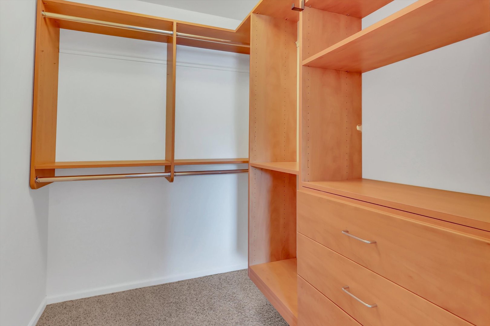 Walk-in closet with light wood built-in shelves, hanging rods, and drawers