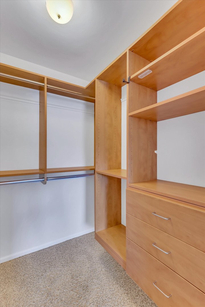 Walk-in closet with light wood built-in shelving, hanging rods, and drawers.