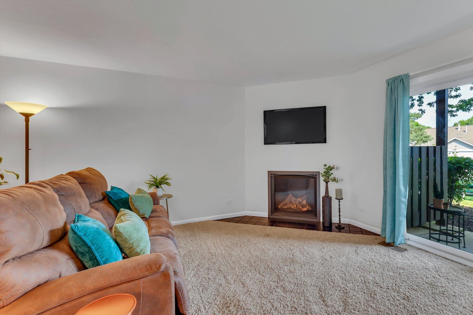Living room with a tan sofa, corner fireplace, and sliding glass door to a balcony.