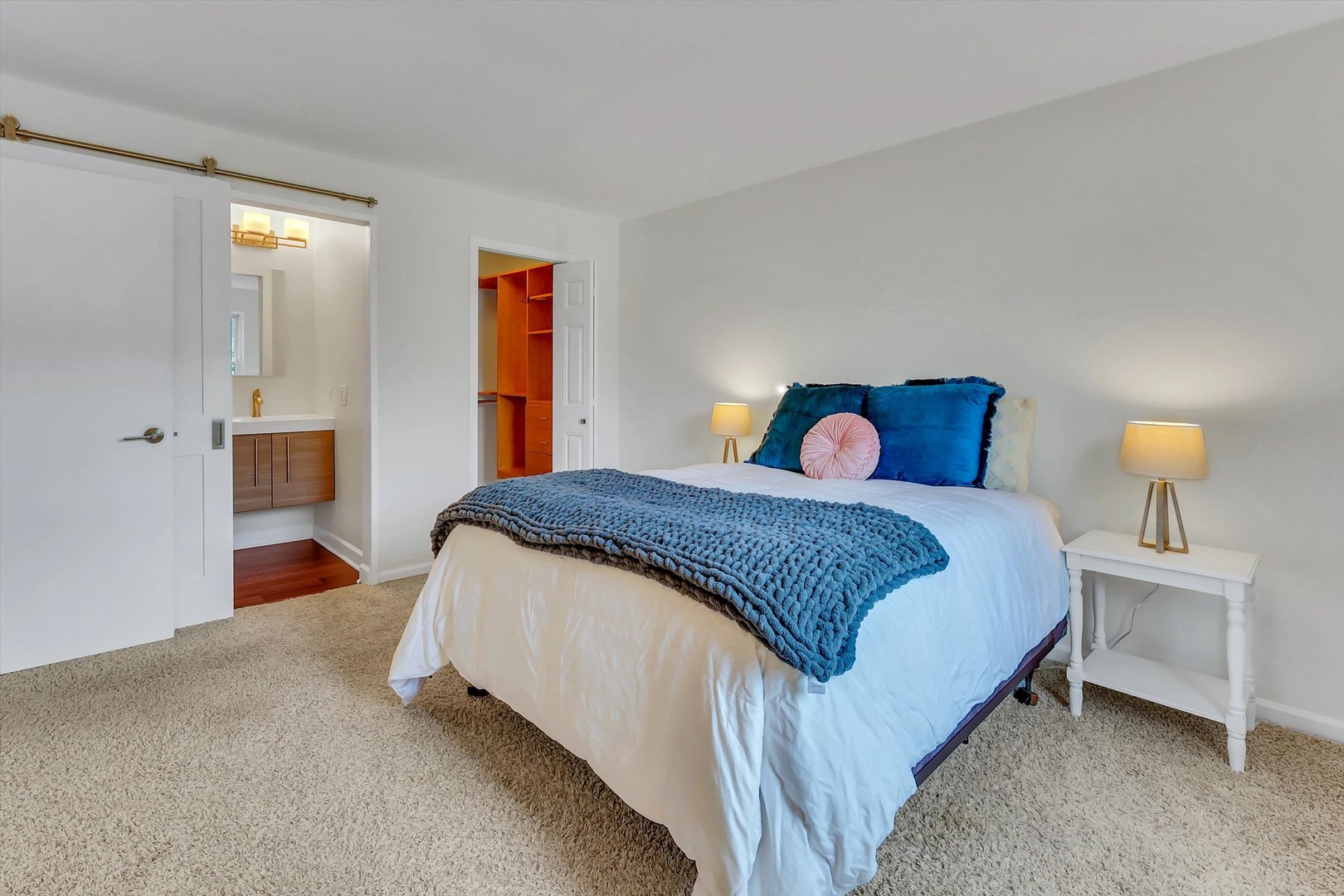 Bedroom with a blue throw-covered bed, an adjoining bathroom, and open closet shelving.
