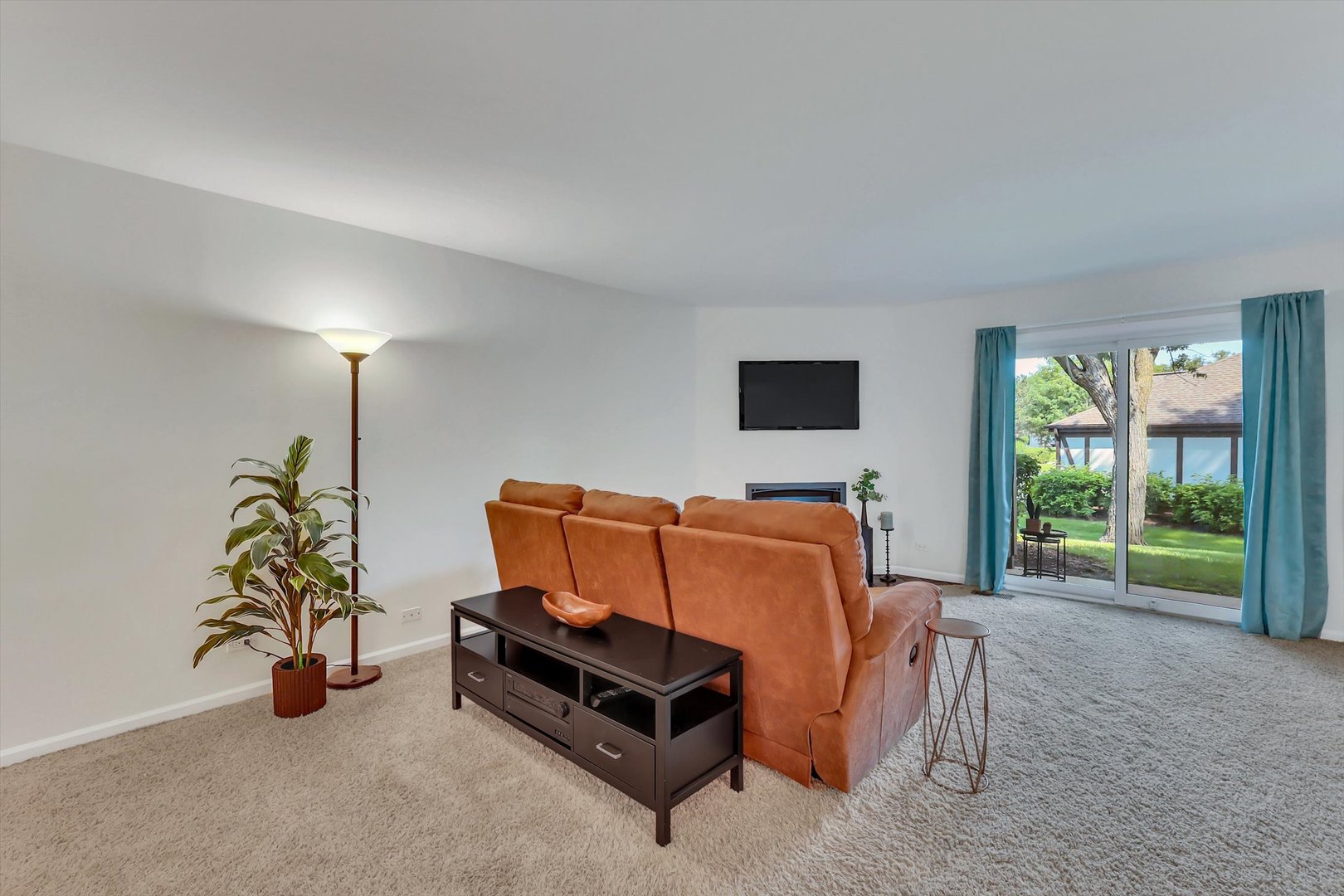 Living room with rust-colored sectional, beige carpet, and sliding glass doors overlooking a green lawn.