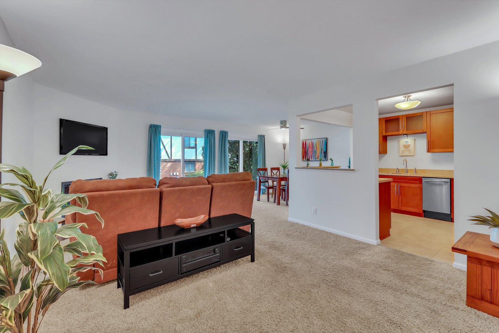 Living room with rust-colored sectional, blue curtains, and open views to the dining area and kitchen.