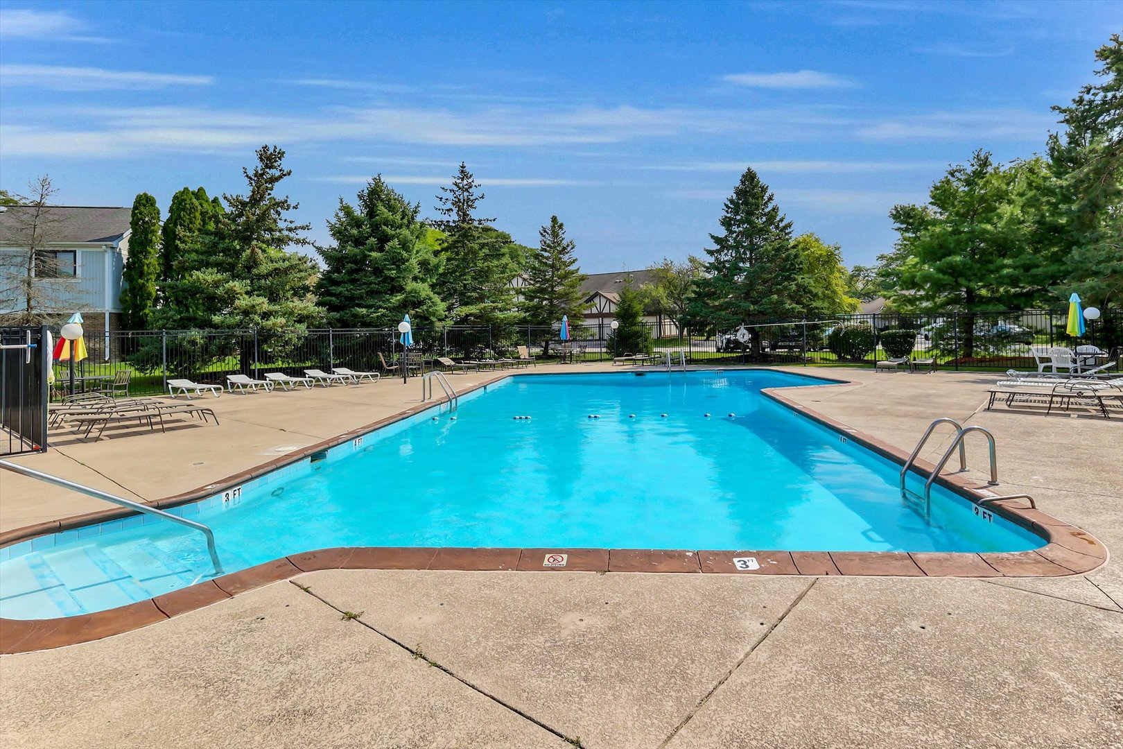 Community swimming pool with lounge chairs and colorful umbrellas on a sunny day.