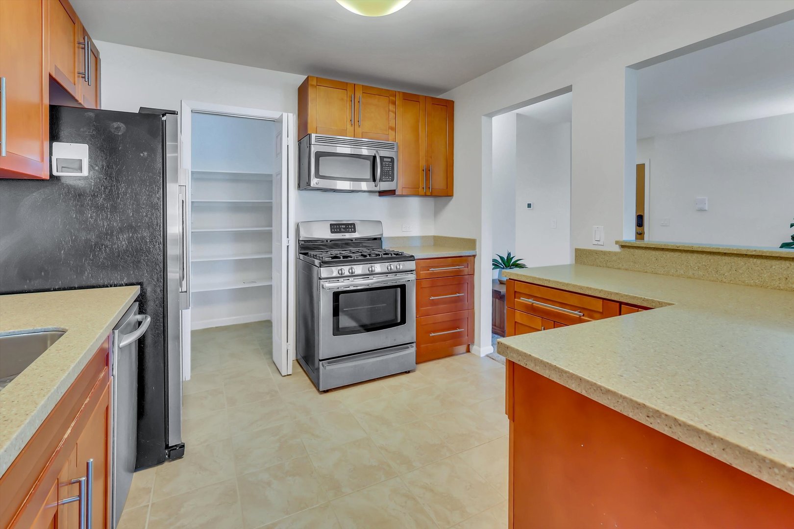 Kitchen with warm wood cabinets, beige counters, stainless appliances, and an open pantry.